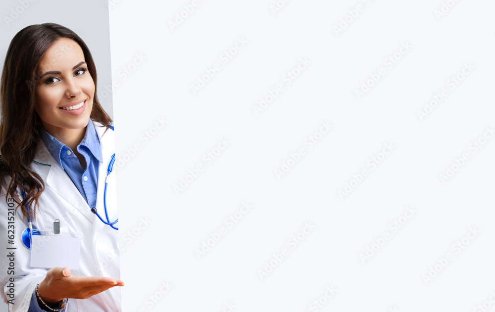 Portrait of happy smiling female doctor showing empty signboard with copy space empty area for some text, over grey. Young brunette beautiful woman in medical, clinic, healthcare studio concept. Portrait of happy smiling female doctor showing empty signboard with copy space empty area for some text, over grey. Young brunette beautiful woman in medical, clinic, healthcare studio concept.