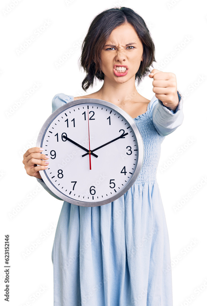 Young beautiful girl holding big clock annoyed and frustrated shouting with anger, yelling crazy with anger and hand raised Young beautiful girl holding big clock annoyed and frustrated shouting with anger, yelling crazy with anger and hand raised