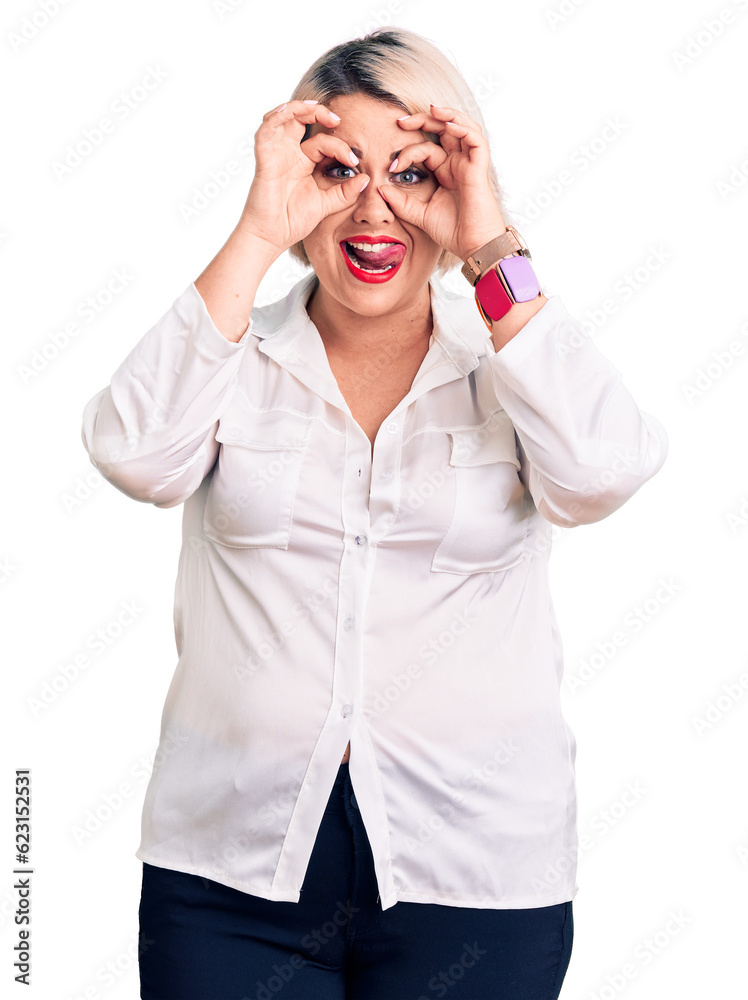 Young blonde plus size woman wearing casual shirt doing ok gesture like binoculars sticking tongue out, eyes looking through fingers. crazy expression. Young blonde plus size woman wearing casual shirt doing ok gesture like binoculars sticking tongue out, eyes looking through fingers. crazy expression.