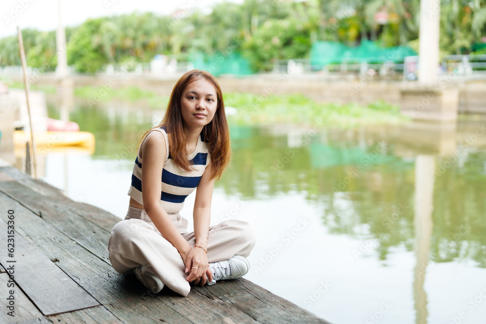 Cute Asian girl with long hair wearing short sleeves Sit and relax in spare time at the pier. By the river on weekends with a smiling face A rural canal with clear water