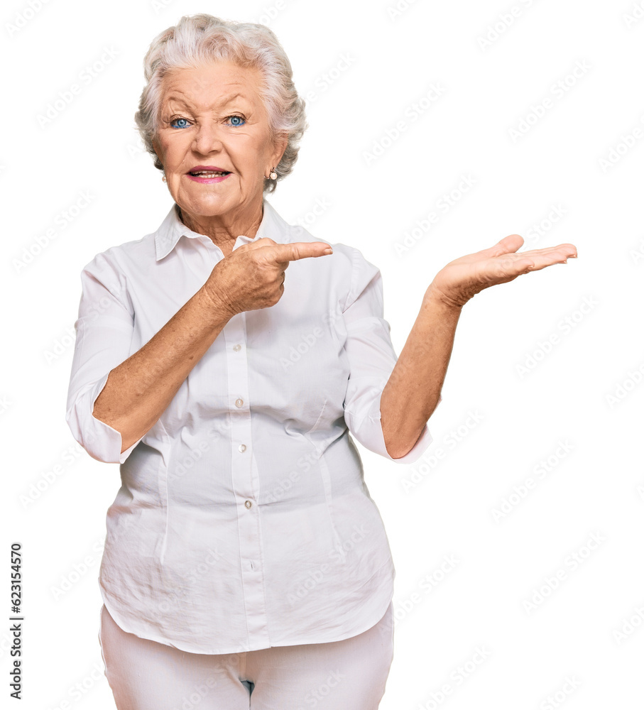 Obraz premium Senior grey-haired woman wearing casual clothes amazed and smiling to the camera while presenting with hand and pointing with finger.