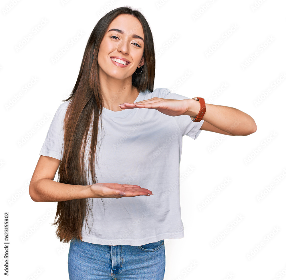 Young hispanic girl wearing casual white t shirt gesturing with hands showing big and large size sign, measure symbol. smiling looking at the camera. measuring concept. Young hispanic girl wearing casual white t shirt gesturing with hands showing big and large size sign, measure symbol. smiling looking at the camera. measuring concept.
