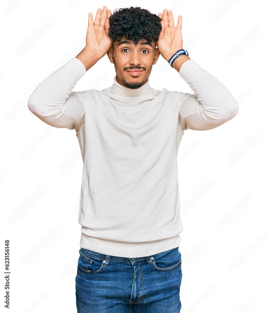 Young arab man wearing casual winter sweater doing bunny ears gesture with hands palms looking cynical and skeptical. easter rabbit concept. Young arab man wearing casual winter sweater doing bunny ears gesture with hands palms looking cynical and skeptical. easter rabbit concept.