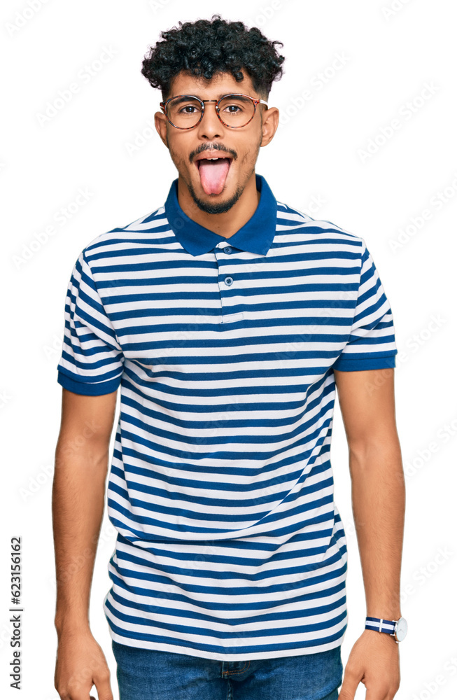 Young arab man wearing casual clothes and glasses sticking tongue out happy with funny expression. emotion concept. Young arab man wearing casual clothes and glasses sticking tongue out happy with funny expression. emotion concept.