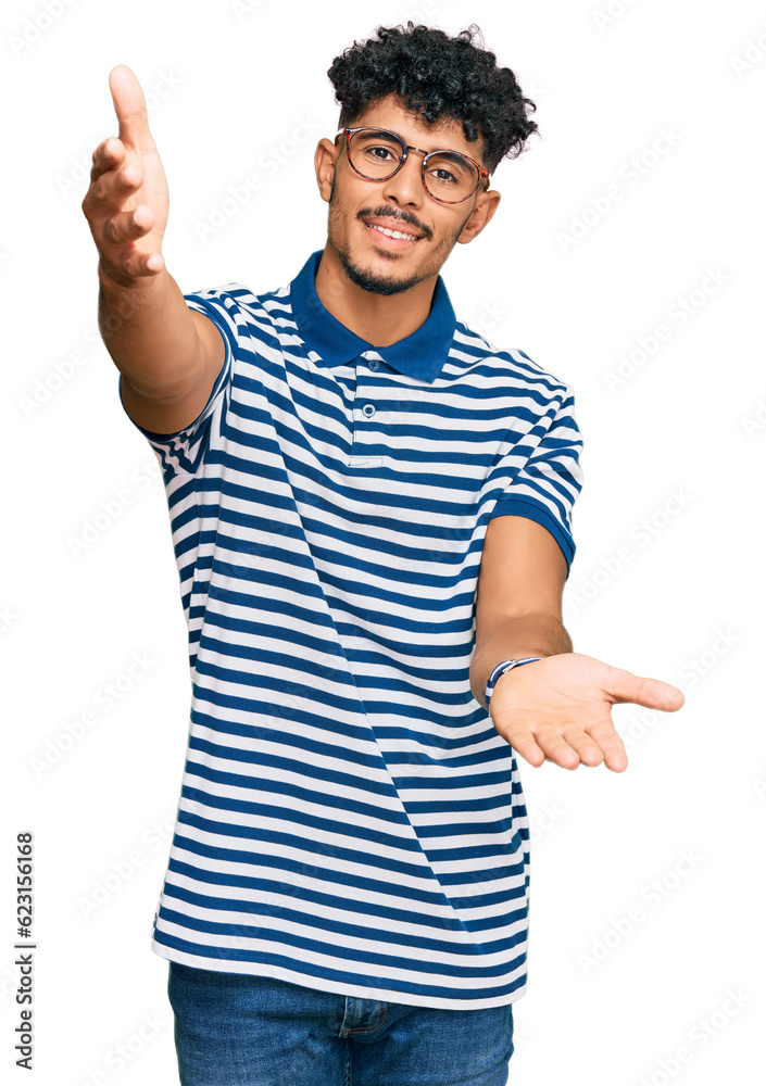 Young arab man wearing casual clothes and glasses looking at the camera smiling with open arms for hug. cheerful expression embracing happiness. Young arab man wearing casual clothes and glasses looking at the camera smiling with open arms for hug. cheerful expression embracing happiness.