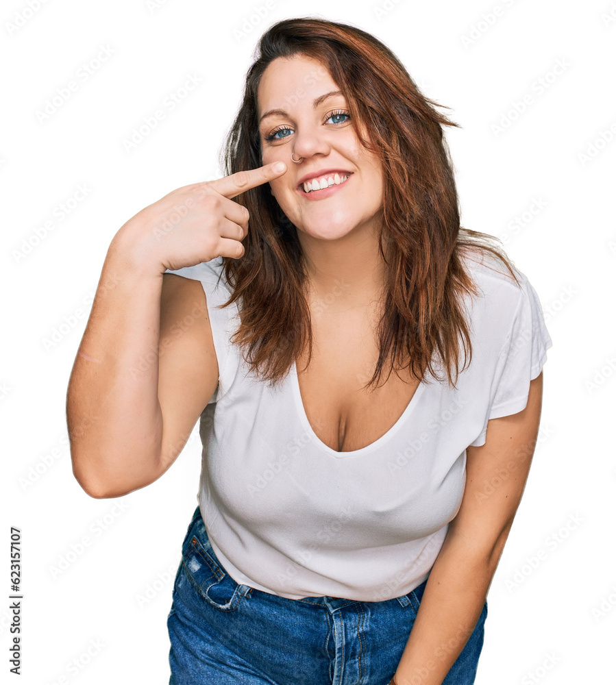 Young plus size woman wearing casual white t shirt pointing with hand finger to face and nose, smiling cheerful. beauty concept Young plus size woman wearing casual white t shirt pointing with hand finger to face and nose, smiling cheerful. beauty concept