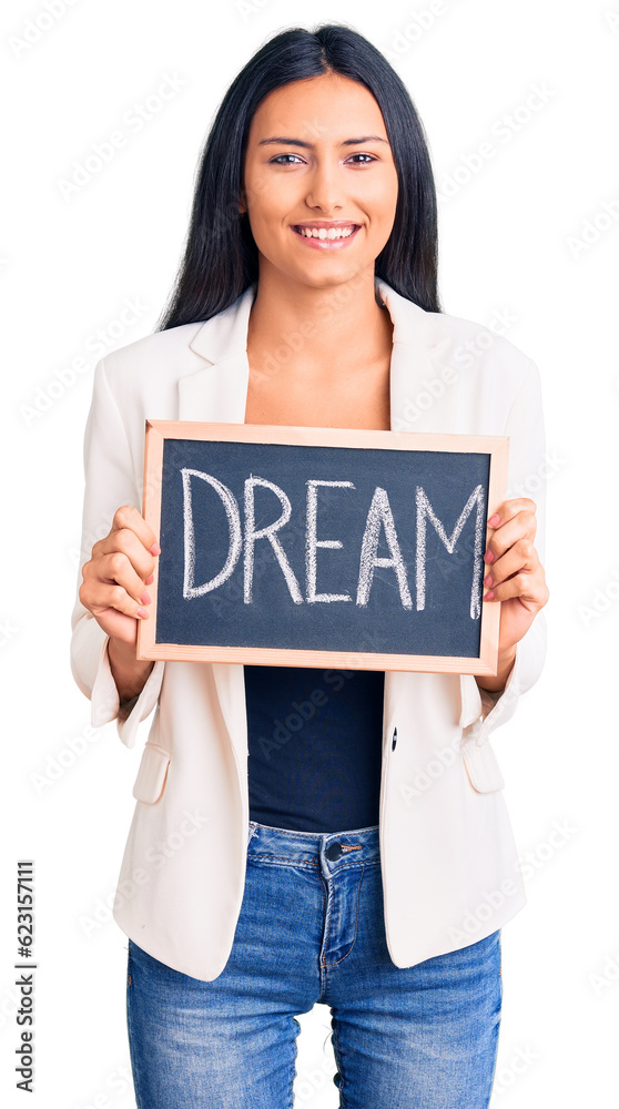 Young beautiful latin girl holding blackboard with dream word looking positive and happy standing and smiling with a confident smile showing teeth Young beautiful latin girl holding blackboard with dream word looking positive and happy standing and smiling with a confident smile showing teeth