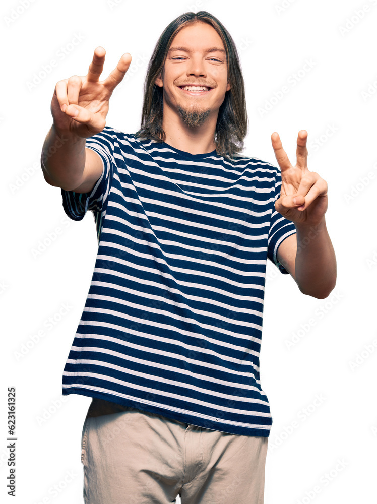 Handsome caucasian man with long hair wearing casual striped t-shirt smiling looking to the camera showing fingers doing victory sign. number two.