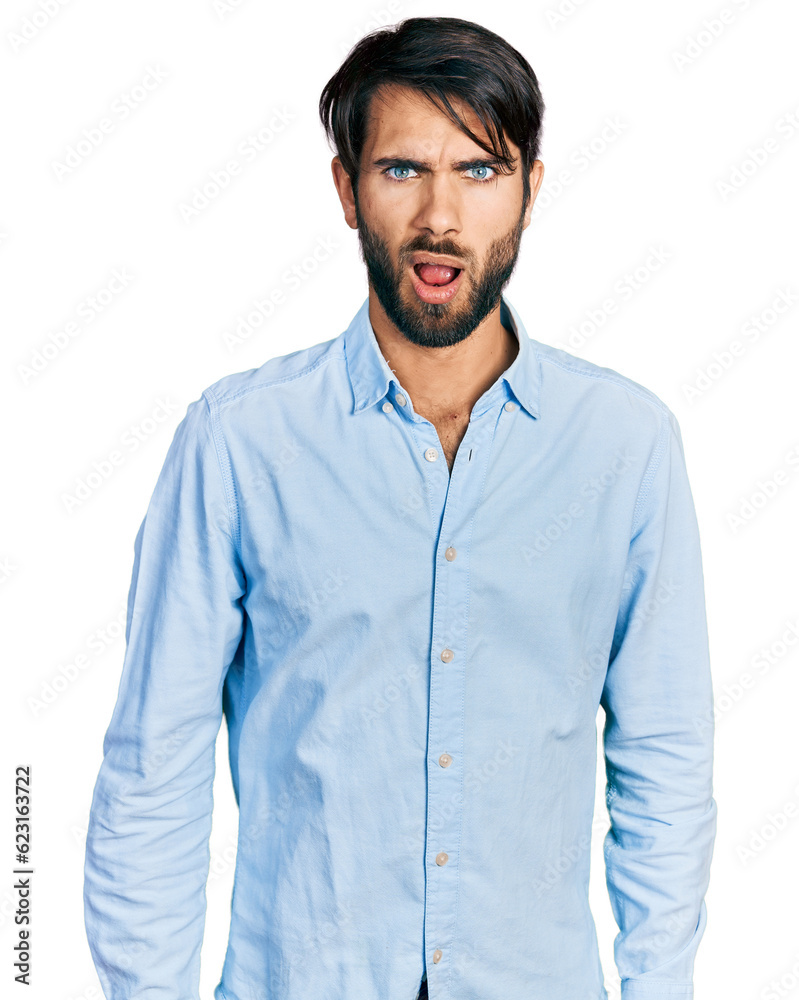 Hispanic man with blue eyes wearing business shirt in shock face, looking skeptical and sarcastic, surprised with open mouth
