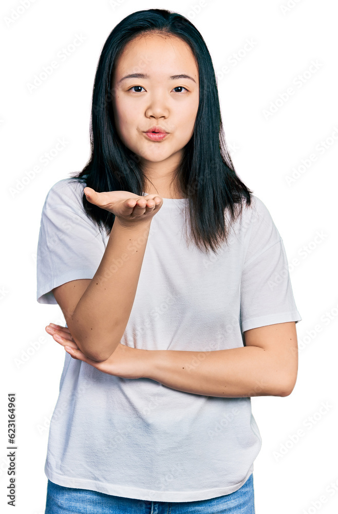 Young chinese woman wearing casual white t shirt looking at the camera blowing a kiss with hand on air being lovely and sexy. love expression. Young chinese woman wearing casual white t shirt looking at the camera blowing a kiss with hand on air being lovely and sexy. love expression.