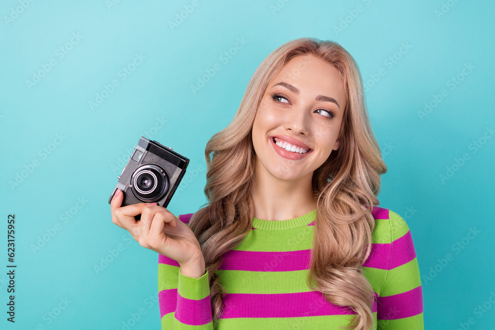 Photo of cunning tricky woman curly hairstyle dressed striped sweatshirt hold camera look empty space isolated on teal color background Photo of cunning tricky woman curly hairstyle dressed striped sweatshirt hold camera look empty space isolated on teal color background
