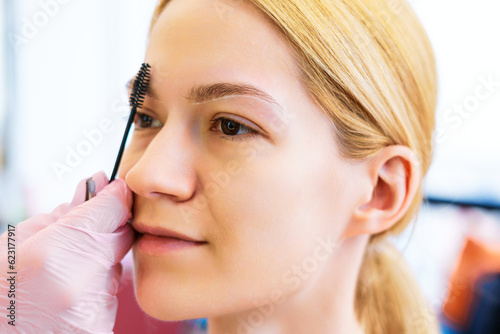 Portrait of a young girl who is combing the hairs on her eyebrows with a black brush. Professional skin care