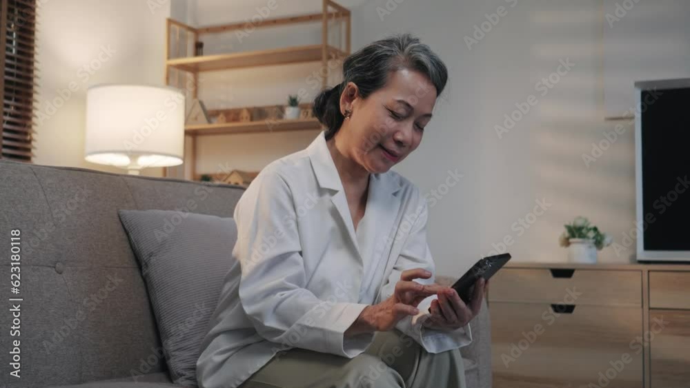 happy senior woman uses phone for online communication, sitting on sofa at home in the evening and smiling happy senior woman uses phone for online communication, sitting on sofa at home in the evening and smiling