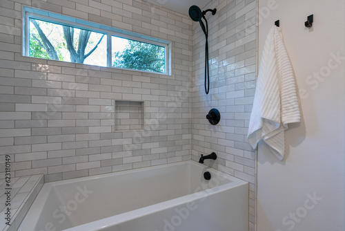 Detail of new tile shower with black faucets, deep tub and picture window. 