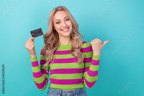 Portrait of optimistic adorable girl wear stylish clothes hold card directing at offer empty space isolated on blue color background