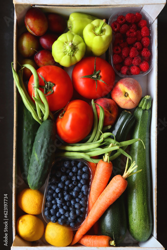 Wooden crate full of healthy seasonal fruit and vegetable. Top view, dark background.