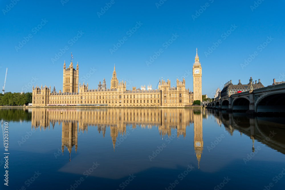 Photo of the entire English Parliament next to Big Ben. Photo taken from the other side of the river, with the reflection of the entire parliament in the river water. On a sunny day. Photo of the entire English Parliament next to Big Ben. Photo taken from the other side of the river, with the reflection of the entire parliament in the river water. On a sunny day.
