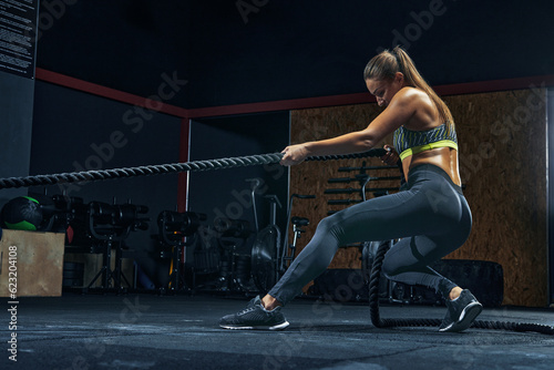 Full-length shot of Power woman functional training with black rope at a gym