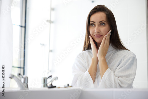 young woman looking at mirror and touching face in bathroom