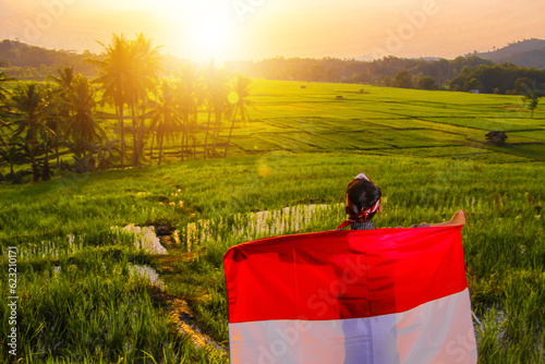 boy waving Indonesian red and white flag with a view of rice fields in the afternoon, against the backdrop of natural optical talent