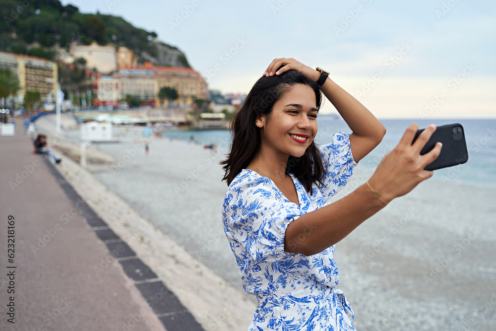 Beautiful smiling young woman takes selfie at the Promenade des Anglais in Nice, France