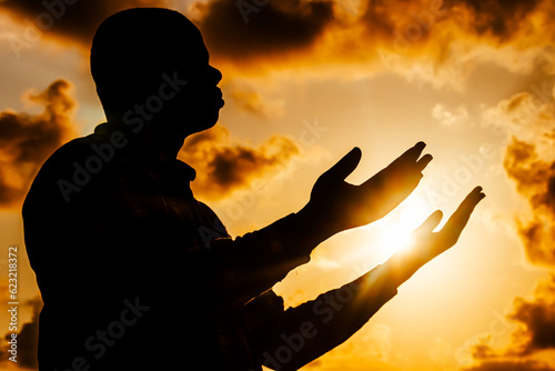 An evocative image capturing the silhouette of a man, his silhouette silhouetted against the fiery solstice sky, as he engages in spiritual connection through prayer.