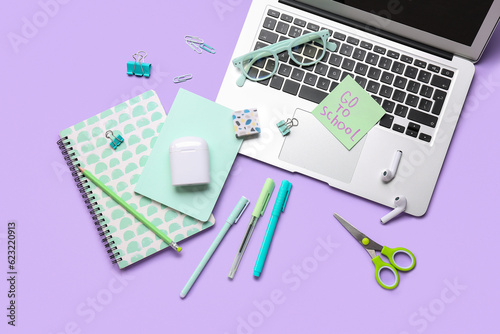 Sticky note with text GO TO SCHOOL, different stationery, laptop and earphones on lilac background
