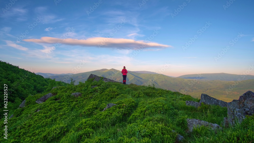 A beautiful girl in a red jacket admires a sunny morning in the mountains. Summer mountain landscape in the Carpathians
