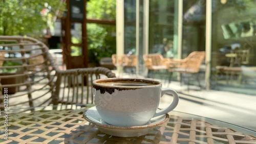 A close-up of cup of black coffee americano on the table of a cafe terrace. Atmosphere of a city coffee house terrace on a warm summer sunny day in the bokeh background. Lifestyle horizontal video.