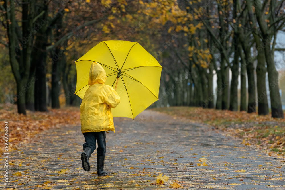 Child in yellow raincoat with an umbrella in his hands runs through