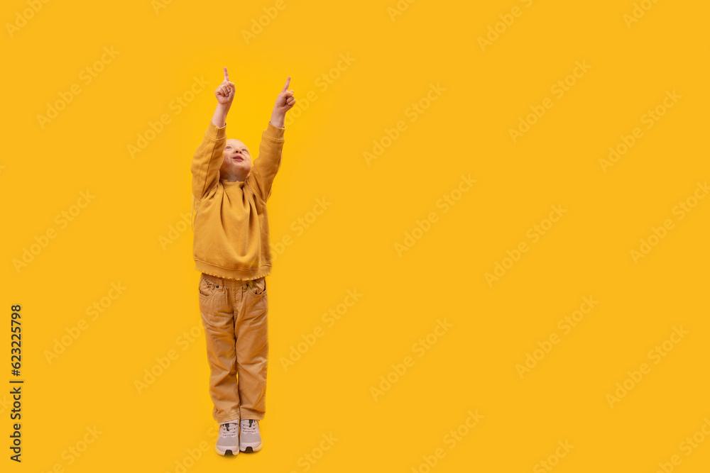 Preschool girl raised hands up and points index fingers up. Copy space, mock up. Vertical frame, child in yellow clothes