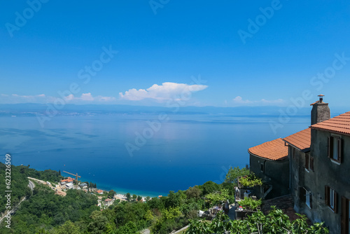 A panoramic view from above of the shore along Moscenicka Draga, Croatia. Few houses on the side. A small town located on the shore of the Mediterranean Sea. Lush green hills along the hills.
