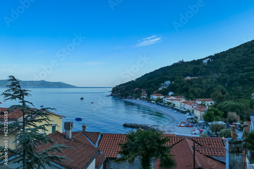 A panoramic view of the shore along Moscenicka Draga, Croatia. There is a small town located on the shore of the Mediterranean Sea. Few boats crossing the calm sea. Green hills in the back. Sunny day. © Chris