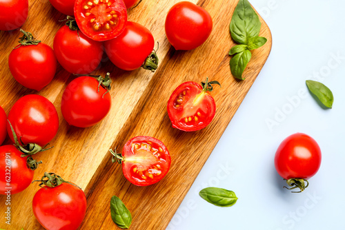 Wooden board with fresh cherry tomatoes and basil on blue background
