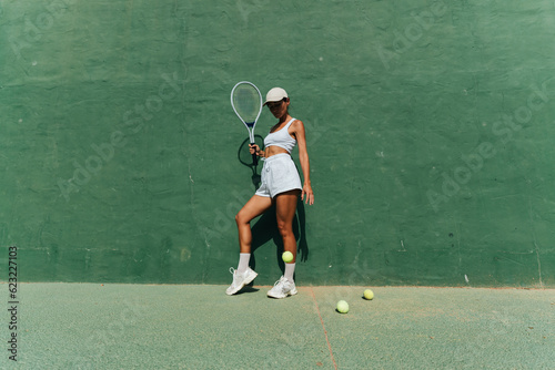 beautiful girl in a cap plays tennis on the tennis court against the background of a green wall