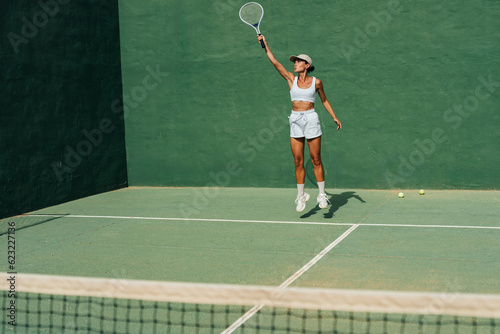 beautiful girl in a cap plays tennis on the tennis court against the background of a green wall