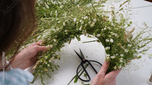 Floristic master class on weaving flower wreath for feast of Ivan Kupala.Woman weaves wreath of fresh field herbs and flowers,pagan symbol,solstice day.Rustic style.Wreath of daisies and herbs,summer.