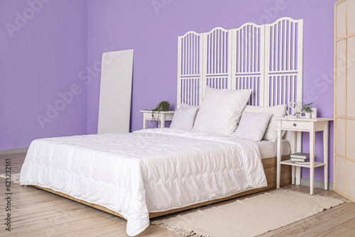 Interior of stylish bedroom with comfortable bed  white pillows  bedside tables and folding screen