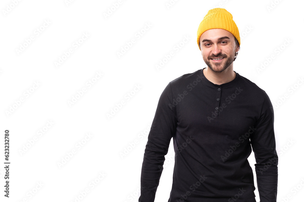 young brutal male model dressed in a black jacket and a yellow hat is smiling on a white background with copy space