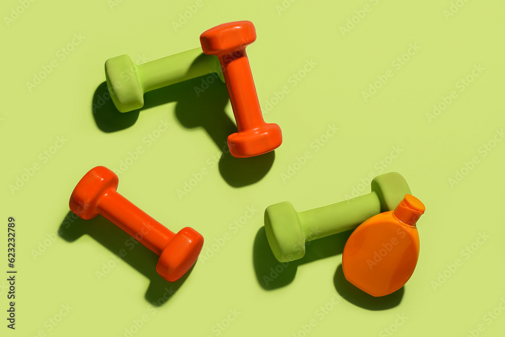 Composition with bottle of sunscreen cream and dumbbells on color background Composition with bottle of sunscreen cream and dumbbells on color background