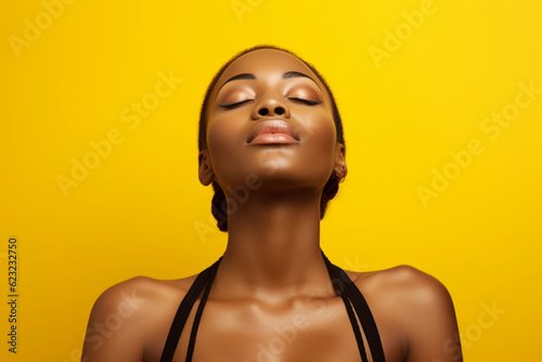 Beautiful African American woman with braids in lingerie with closed eyes against yellow background