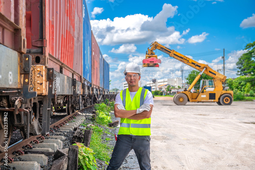 a civil engineer man holding his arm between railway contrainer car and container froklift with blue sky background