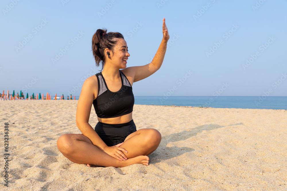 latin woman in sportswear on the beach, sitting waving to the side latin woman in sportswear on the beach, sitting waving to the side