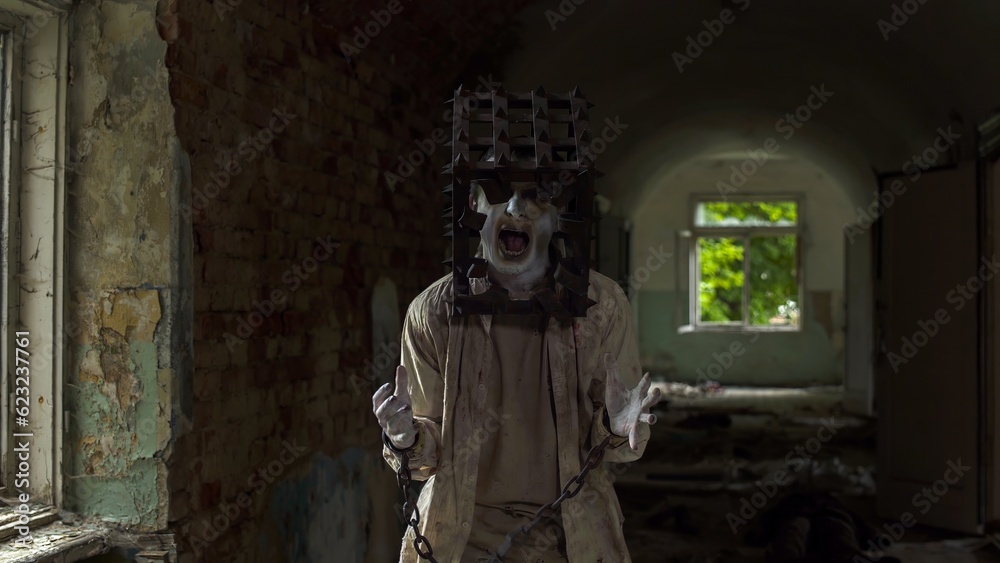 Fototapeta premium Ghost of maniac with cage on his head dragging dead body down corridor of asylum
