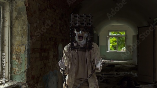 Obraz na plátne Ghost of maniac with cage on his head dragging dead body down corridor of asylum