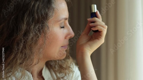 Woman sniffing perfume on her wrist. Half-length portrait at the window, aroma oils and natural flavors, oil perfumes