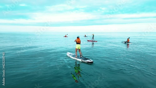 a company of SUP surfers swims on a board with a paddle on the sea at dawn on a beautiful background of calm water and mountains