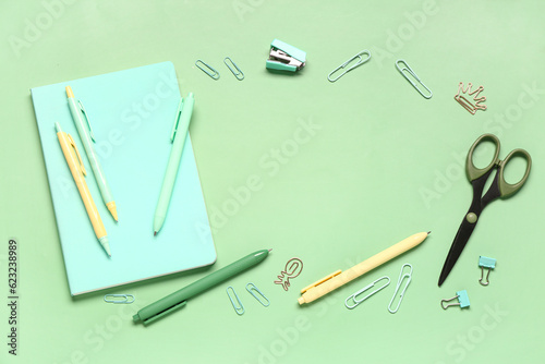 Frame made of notebook with different school stationery on green background