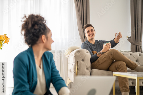 man and woman happy caucasian couple sitting at home chatting and talking in bright room in day real people family concept copy space young adult husband and wife having conversation © Miljan Živković