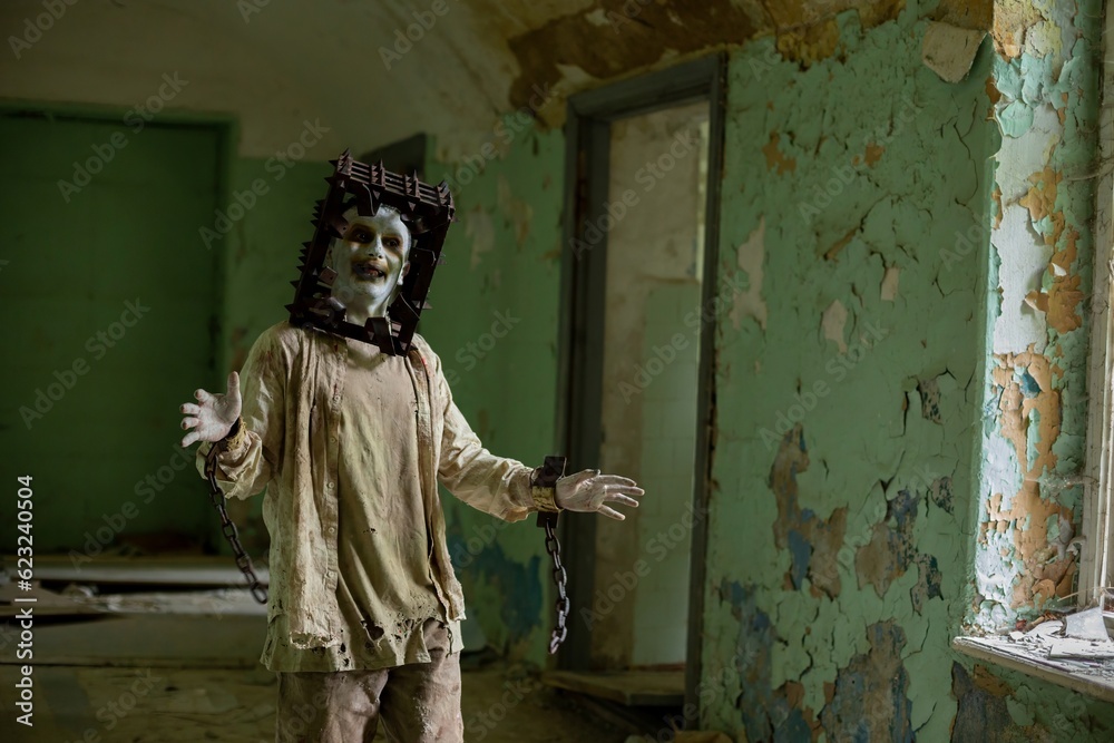 Ghost of maniac with cage on his head walking down corridor of abandoned asylum.
